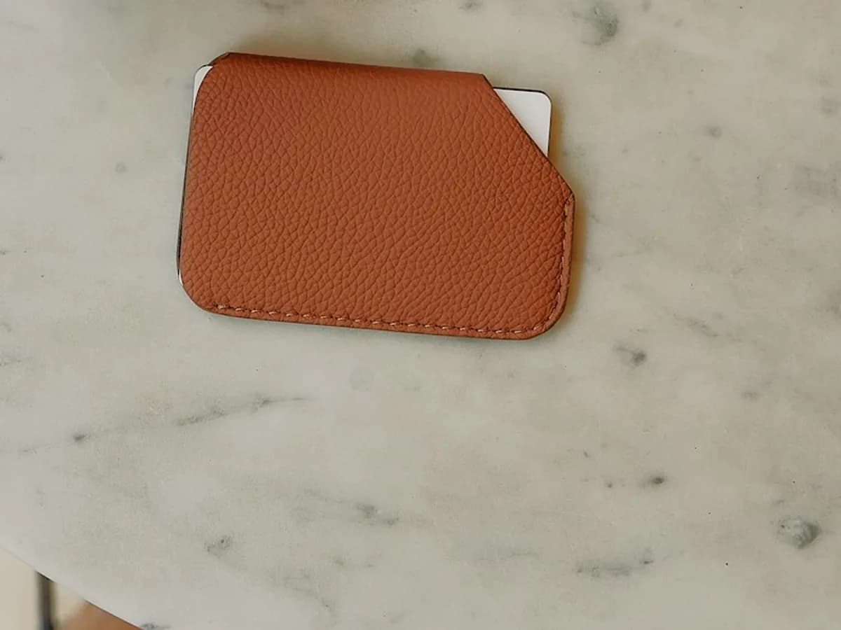 Brown leather card holder with edge stitching on a pale stone tabletop.