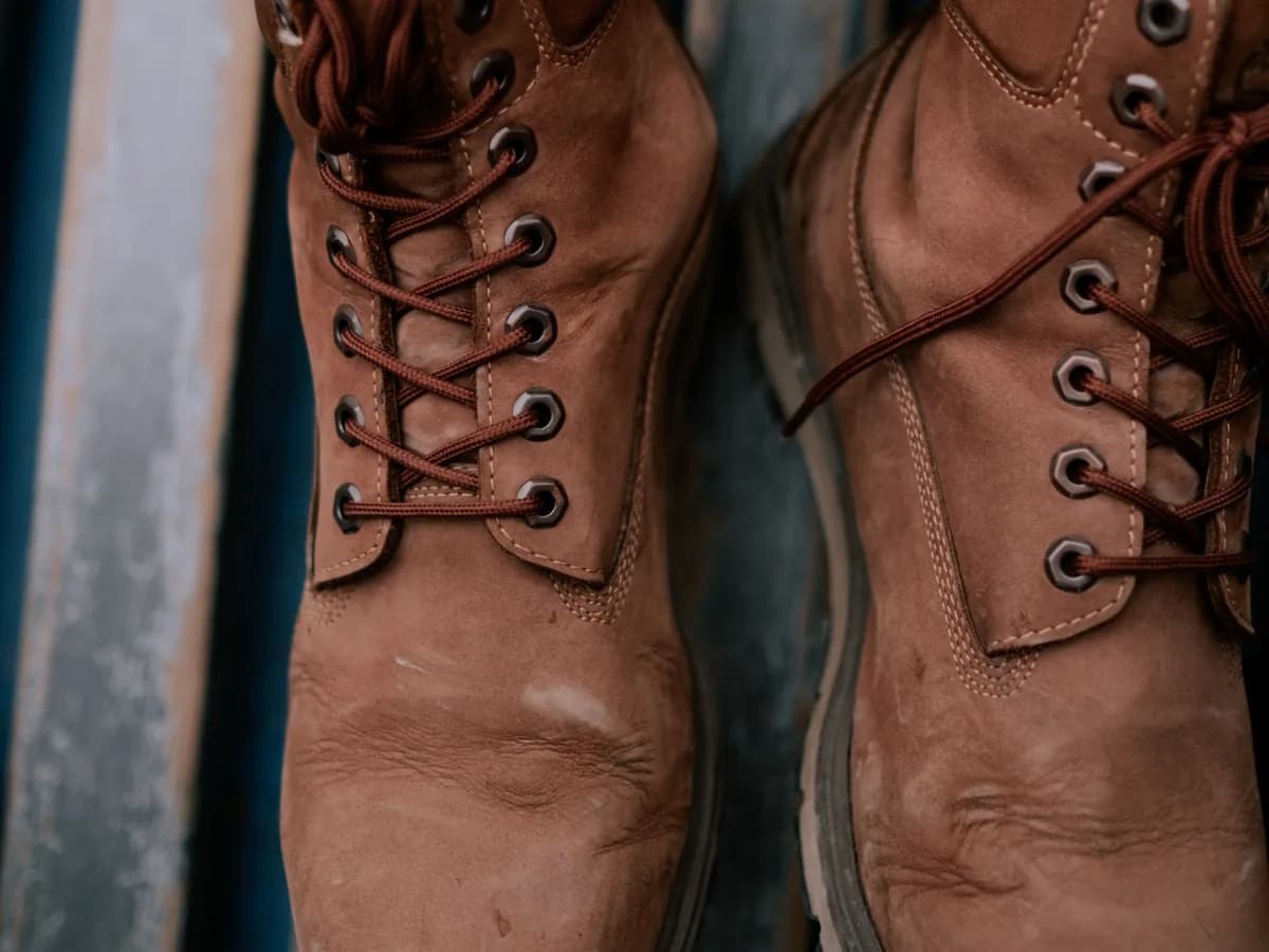 Close-up of brown leather lace-up boots above wooden floorboards.