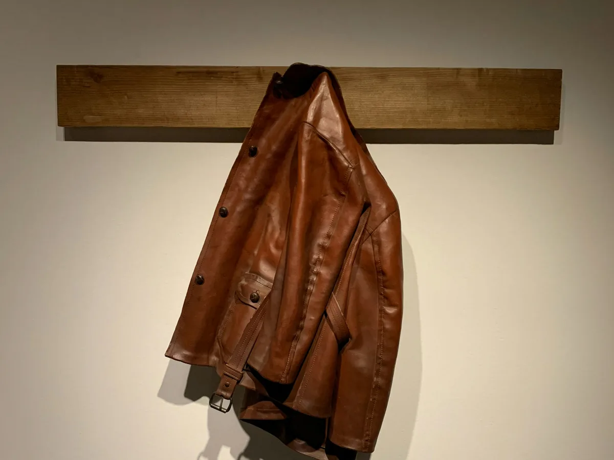 Brown leather jacket hanging from a wooden wall rack.